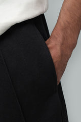 Close-up detail shot of a model's hand resting inside the side pocket of black fleece-lined winter trousers, highlighting the fabric texture, side seam stitching, and elasticated waistband worn under a white top.