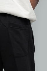 Close-up detail shot showing the back patch pocket, waistband stitching, and fabric texture of black winter trousers, worn with a white top against a light grey background.