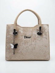 A beige velvet handbag with gold 'Dior' logo and a butterfly charm.