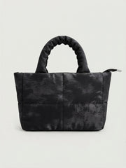 A structured black mini tote bag with an abstract, textured camouflage quilt pattern and ruched handles, viewed from the front against a neutral wall.