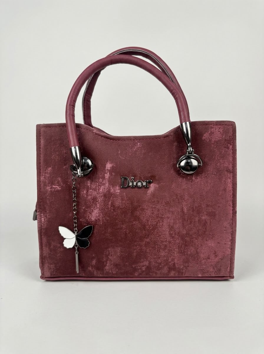 Front view of a burgundy velvet handbag with gold 'Dior' logo and butterfly charm.