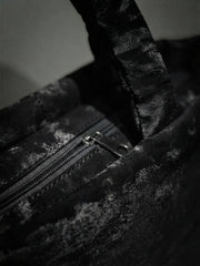 A detailed close-up photograph of the top zipper closure and silver-tone pull tab on the black abstract camo quilted handbag.
