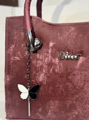 Close-up of 'Dior' logo and butterfly charm on the burgundy velvet bag.
