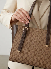 Close-up of a hand holding a brown leather handle attached to a beige and brown monogram tote bag.