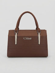 A front view of a brown structured handbag with top handles and vertical silver hardware accents.