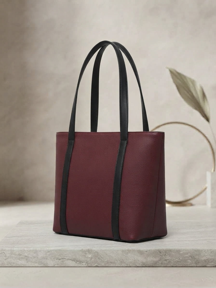 Three-quarter angle of the maroon textured tote bag showcasing its side depth and dual black straps.