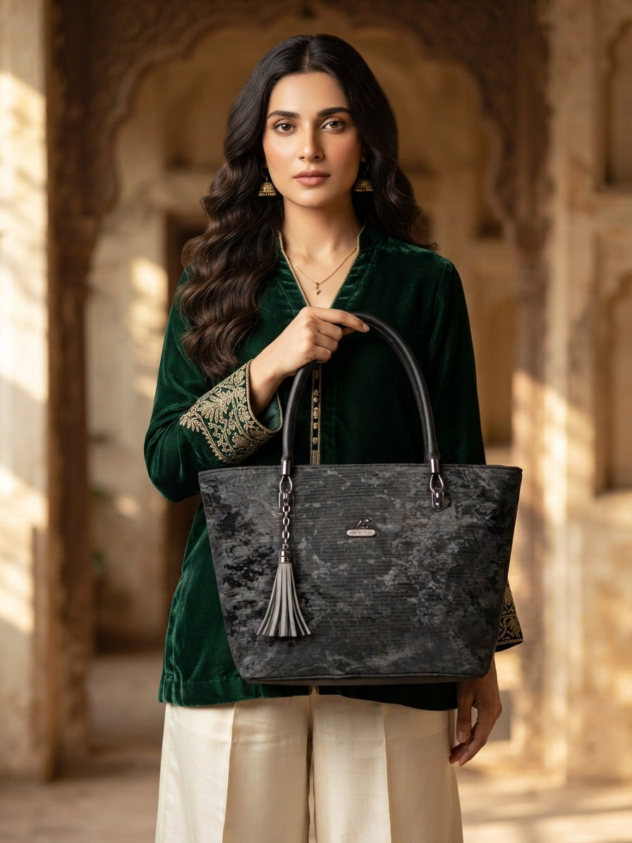 A model in a green top holds the charcoal grey tote bag in an ornate archway.