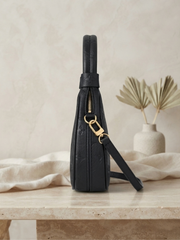 Side profile view of the black embossed Louis Vuitton Loop handbag on a light beige marble surface, showing the bag's depth and strap attachment.
