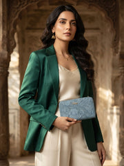 A woman in a green satin blazer and cream pants holds a blue textured wallet.