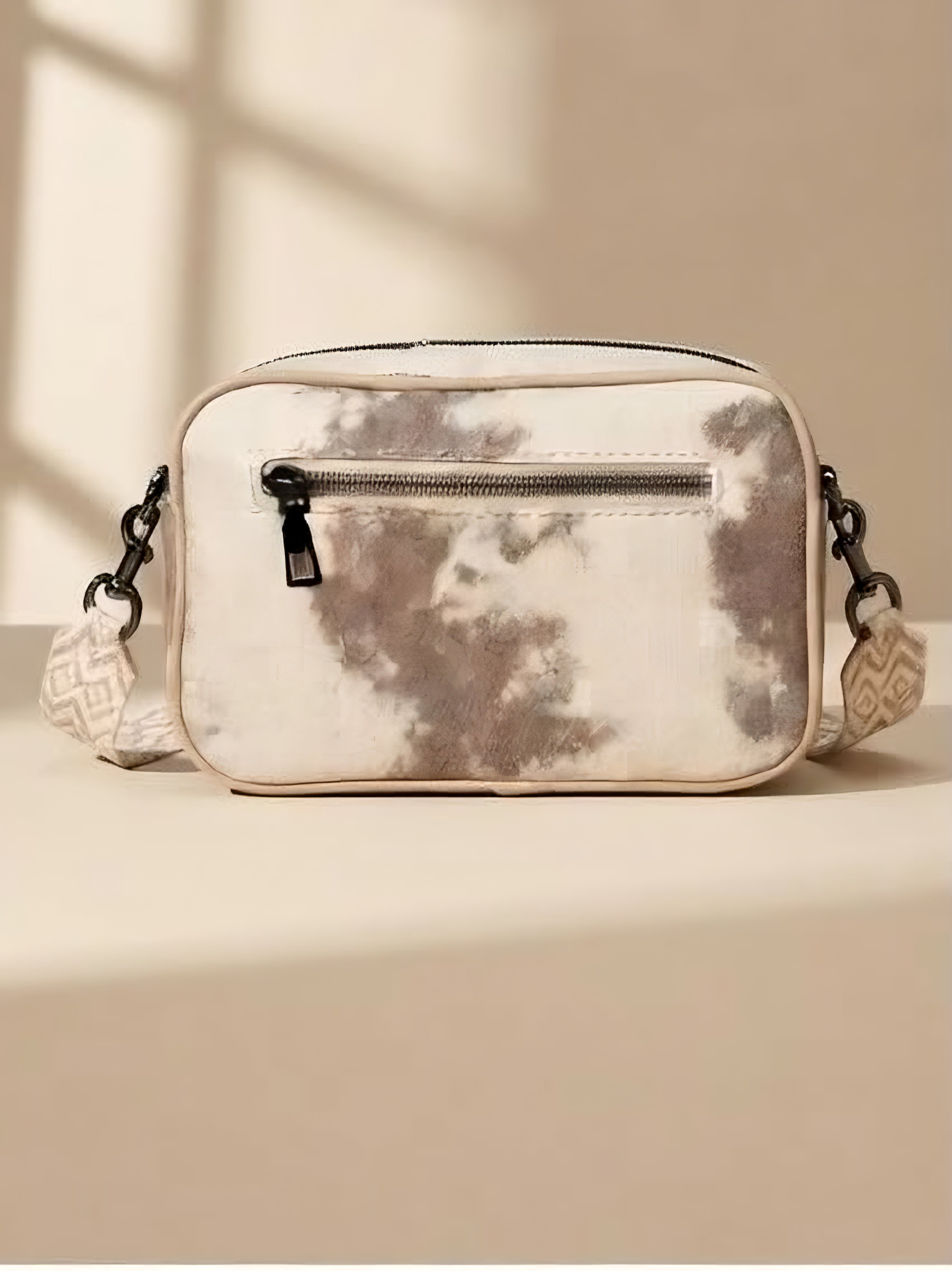 A back side of rectangular bag with a beige and brown tie-dye pattern, featuring a zip pocket and a matching patterned shoulder strap displayed.