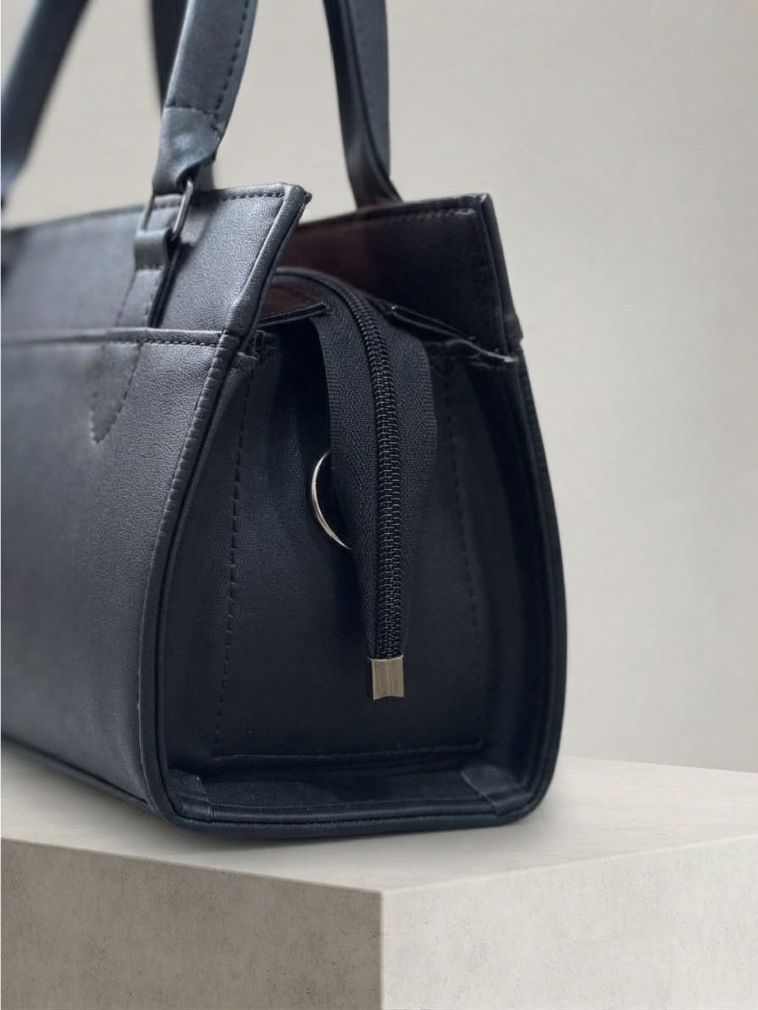 Close-up of the side profile of the black handbag showing the zipper and pull.