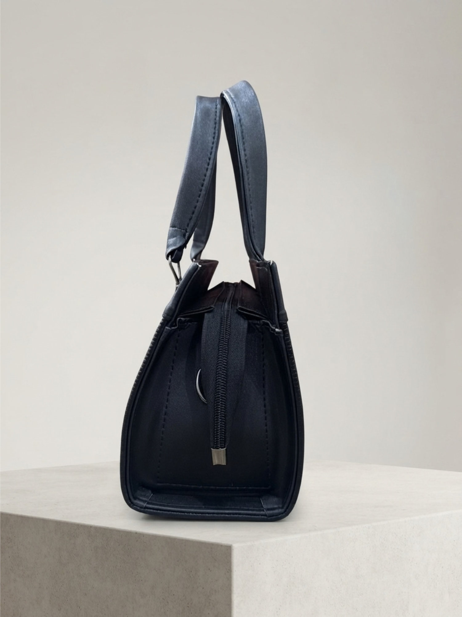 Side profile of the black handbag showing its width and handles against a neutral background.