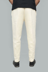 A person shown from the back wearing off-white or cream trousers, a black top, and black shoes against a plain light gray studio background.