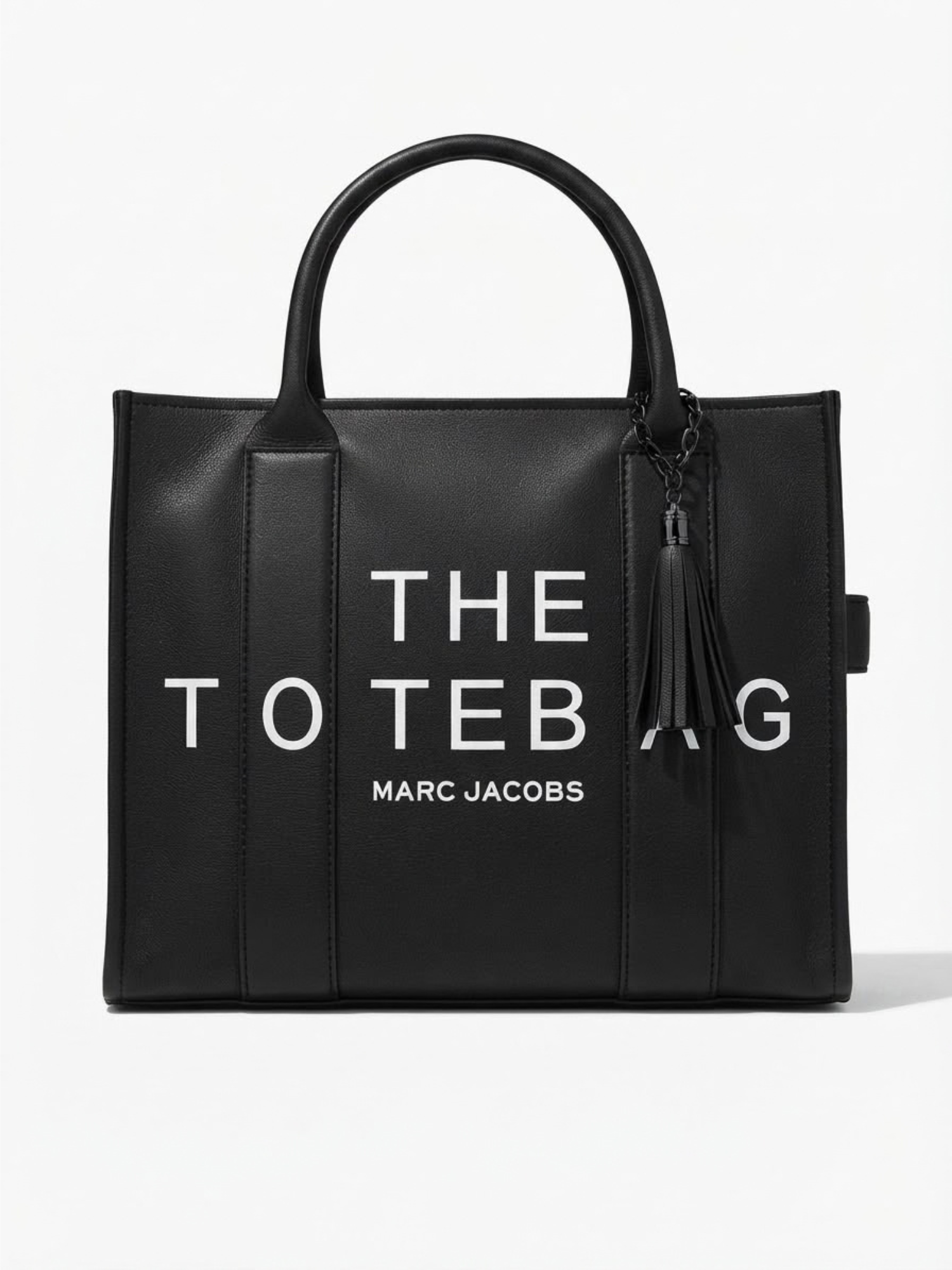 Front view of a structured black leather tote bag featuring white "THE TOTE BAG MARC JACOBS" typography and a matching tassel charm.