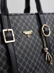 Close-up detail of the gold-tone buckle straps, brand logo badge, and charm keychain on the black patterned tote bag.