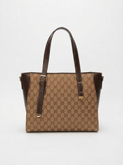 Front view of a beige and brown monogram tote bag with brown leather straps and buckles on a plain white background.