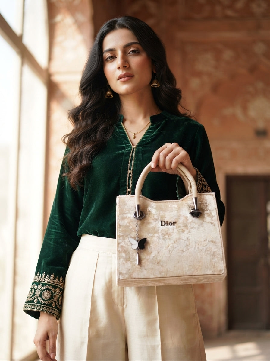 A model in a green velvet top and cream pants holding the beige velvet handbag.