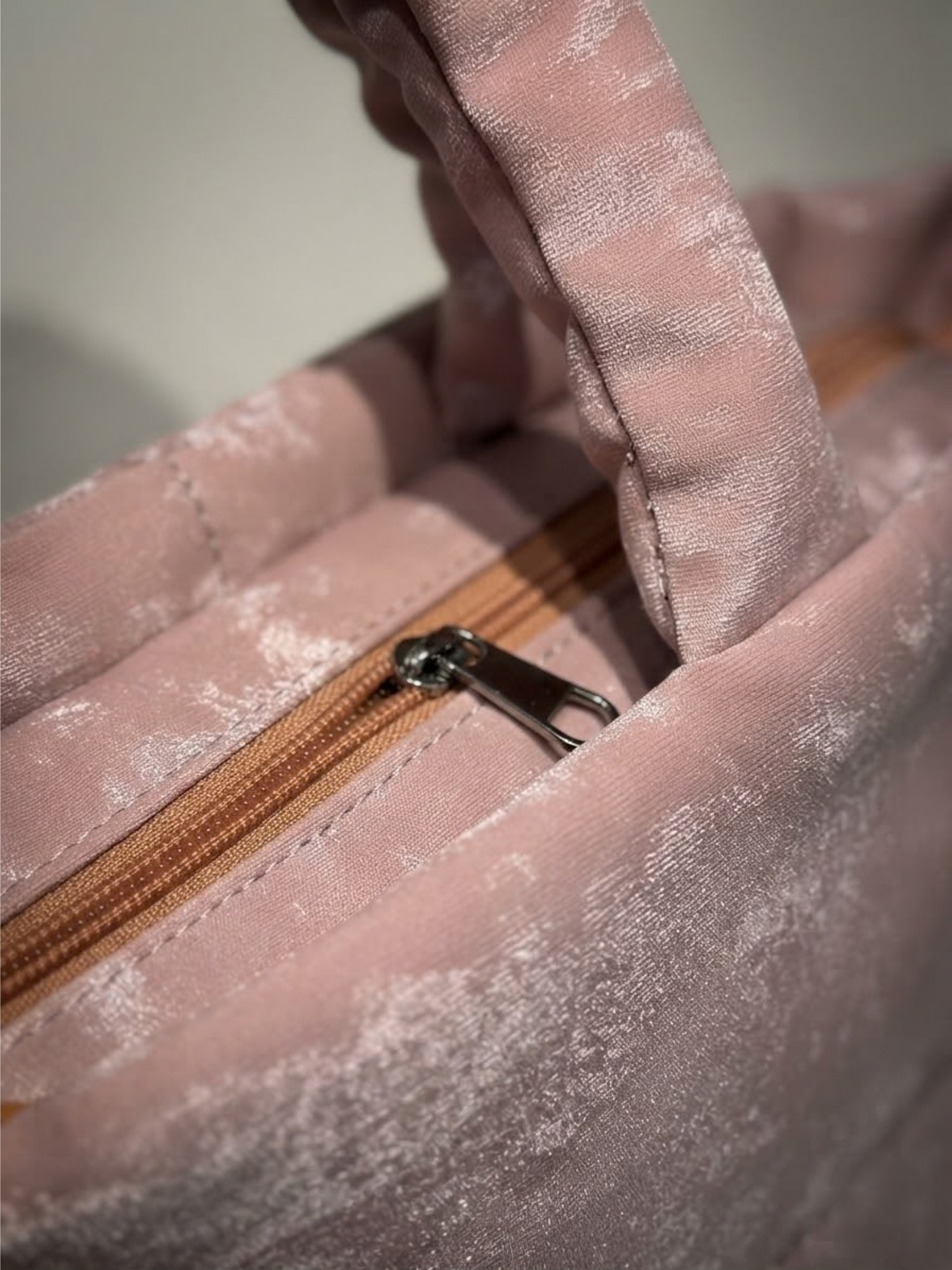 Close-up detail of the zipper closure and plush top handle on the pink textured handbag.