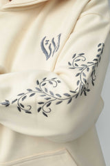 Premium cream oversized hoodie in soft fleece fabric with dark floral embroidery on the sleeve and minimal chest motif.
