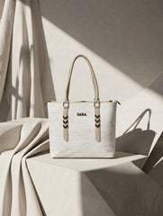 Front view of a white textured leather tote bag with top handles and chevron hardware accents displayed on a minimalist studio podium.