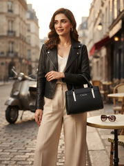 Woman in a Parisian street setting holding the black Chloè handbag, wearing a black leather jacket and beige pants.
